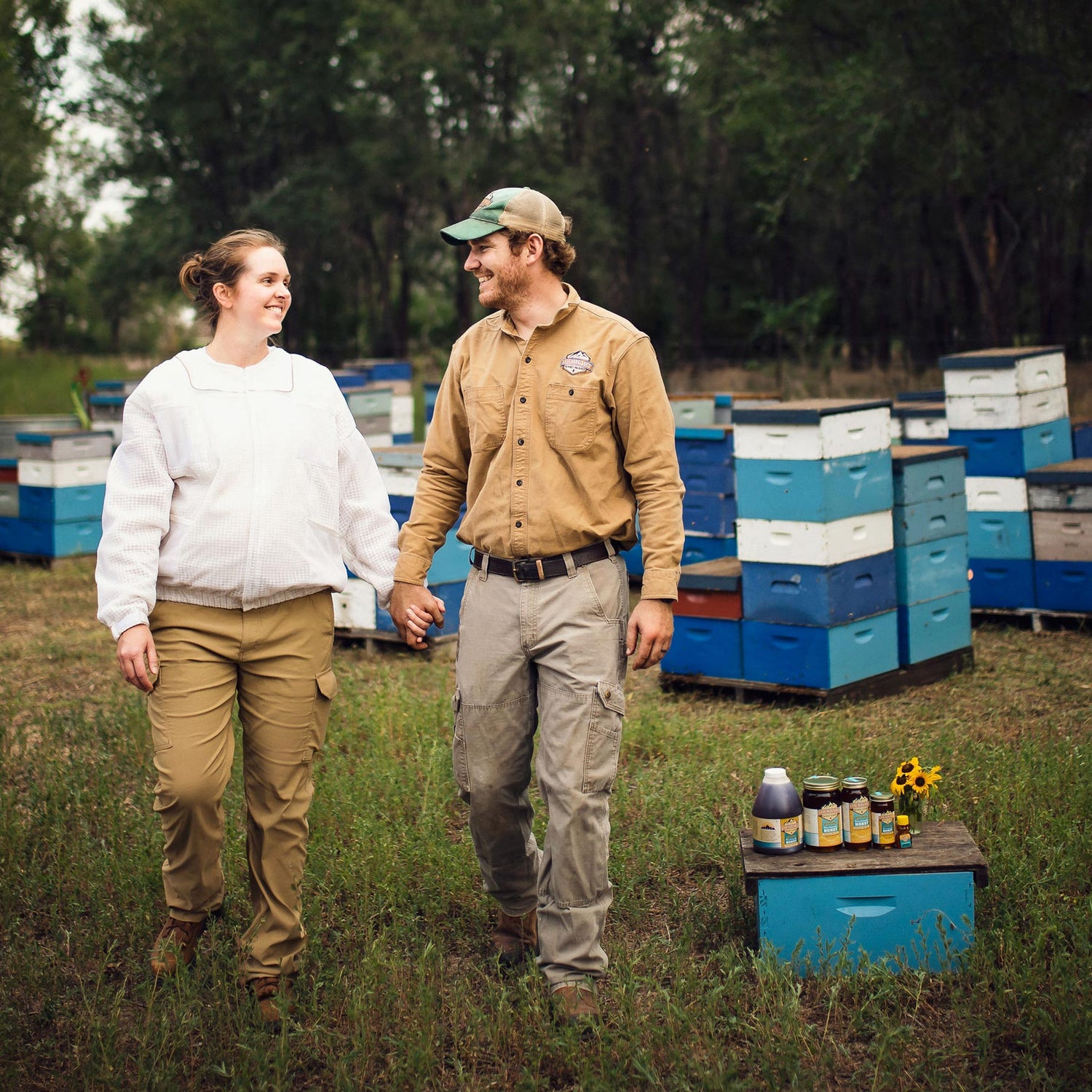 Leo and Laura Lockhart holding hands with bee hives in background